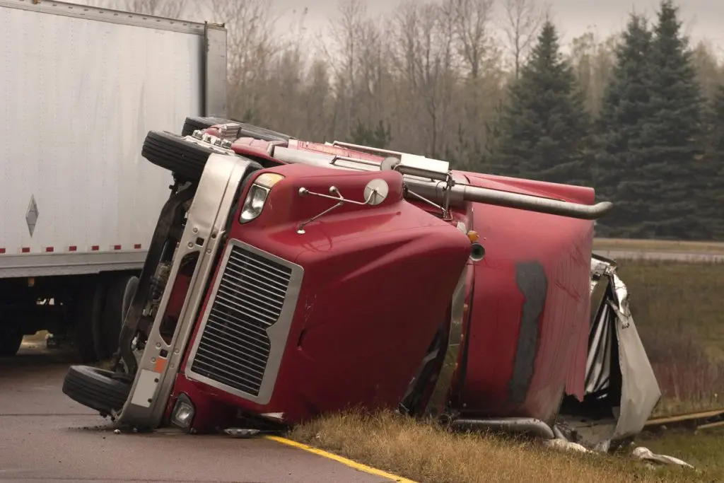 Transport truck crashed with jack knifed trailer lays on side of freeway