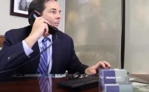 An Allentown Lyft accident attorney at Munley Law takes a call from an injured rideshare passenger seeking legal help. The attorney, seated at a desk in a professional office, listens intently while reviewing case notes on his computer. The calm, focused setting emphasizes the firm’s experience, compassion, and commitment to client care. Subtle branded elements reinforce trust and recognition, while natural light conveys accessibility and openness.