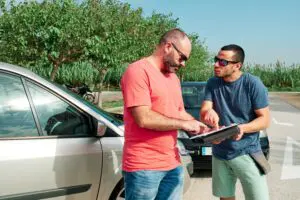 Two drivers exchange information next to their cars after a collision, representing the initial steps in addressing an accident potentially involving uninsured motorists. Munley Law, experienced car accident lawyers in Allentown, PA, guide victims through obtaining an average uninsured motorist settlement. Contact Munley Law at (855) 866-5529 for professional assistance. This image highlights the importance of thorough documentation and insurance information exchange in accident claims.