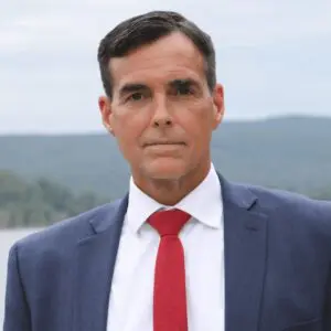 Munley Law offers expert Allentown workers’ compensation lawyer services in Allentown, Pennsylvania. This image shows a lawyer in a blue suit with a red tie, standing outdoors with a scenic background of hills and water, representing the firm’s professional approach to workplace injury cases. Located in Allentown, Munley Law helps injured workers secure fair compensation. Call 570-865-4699 to connect with the Allentown workers’ compensation lawyers at Munley Law for your claim.