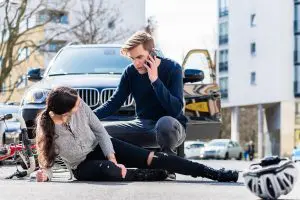 Full length view of a worried young driver calling the ambulance after hitting and injuring accidentally a female bicyclist on a city street