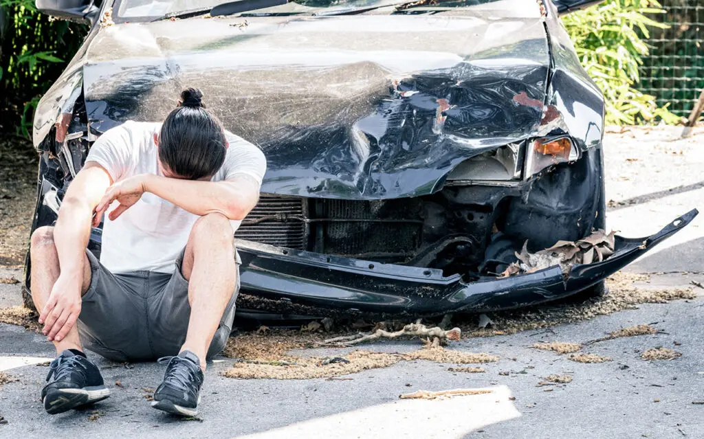 Injury victim sits in front of damaged car after an auto accident in Carbondale