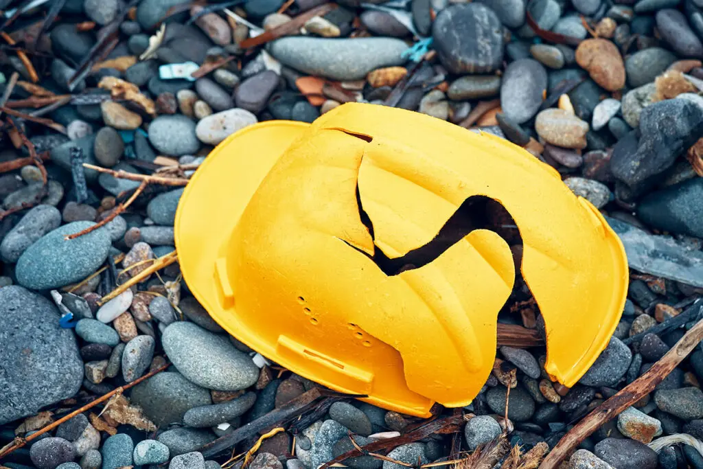 Cracked work helmet on the floor covered with pebble stones. Concept of work accident.