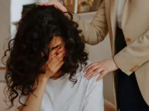 A person visibly distressed, head in hands, being comforted in a professional, empathetic environment, symbolizing emotional trauma often faced by victims after car accidents in Allentown, PA. Munley Law, reachable at (855) 866-5529, provides compassionate legal representation for victims dealing with emotional distress and injuries from car crashes involving uninsured motorists. The indoor setting of the image reinforces the private, supportive assistance clients receive when navigating injury settlements. This depiction emphasizes Munley Law's dedication to supporting the emotional well-being of car crash victims throughout the legal process.