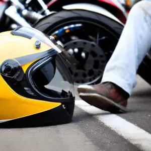 A motorcycle helmet resting on the asphalt beside crash debris, with a blurred police car in the background, representing a motorcycle accident attorney’s work after serious collisions.