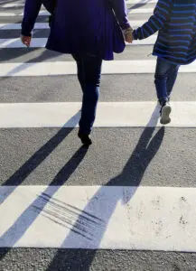 woman and child holding hands crossing pedestrian crosswalk