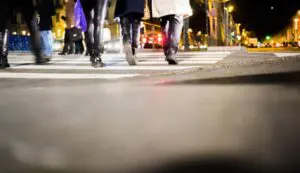 Munley Law offers experienced pedestrian accident attorney services in Pennsylvania, call 855-866-5529 for a free consultation. The image shows a pedestrian crossing sign near an intersection, with reflective elements illuminated in evening lighting. The Pennsylvania roadway environment is portrayed realistically, emphasizing safety concerns and the risk of pedestrian accidents.