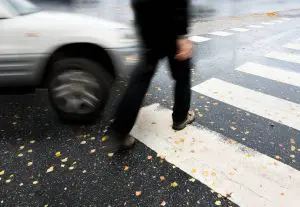 person crossing the street as car comes around corner