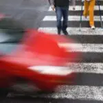 A red SUV is stopped in the middle of a Philadelphia crosswalk, showing visible road scrapes and minor front damage. The scene represents a potential pedestrian collision on a city street. This photo is used by Munley Law’s Philadelphia pedestrian accident attorneys—call 855-866-5529 for representation. The angle highlights the street markings and urban roadway detail in natural daylight.