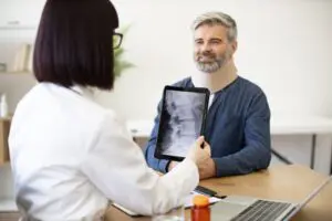 This image shows a detailed medical consultation for a spinal cord injury patient in Allentown, PA, emphasizing Munley Law's commitment to supporting injury victims. A medical professional, holding an X-ray image of a spinal injury, explains treatment and rehabilitation options to the patient, who wears a supportive neck brace. Munley Law's compassionate attorneys assist individuals through these challenging circumstances, guiding them toward securing the compensation needed for extensive medical care. Contact Munley Law in Allentown, PA, at 855-866-5529 for trusted legal guidance in spinal cord injury cases.