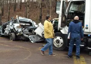 A severe truck collision scene on a Scranton roadway depicting extensive damage to a passenger car following impact with a large commercial truck. Munley Law Personal Injury Attorneys in Scranton, PA, reachable at (570) 865-4699, specializes in representing victims of similar truck accidents. The image shows crushed vehicle metal, displaced car parts, and significant structural damage highlighting the severe consequences of truck accidents. This type of scene is commonly investigated by Munley Law to secure compensation for truck accident victims.