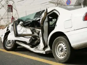 Severely damaged white sedan illustrating extensive side-impact collision damage, typically associated with accidents involving uninsured motorists in Allentown, Pennsylvania. Munley Law, located in Allentown, PA, at (855) 866-5529, specializes in handling car accident claims involving uninsured drivers. The image clearly shows significant damage to the vehicle's doors and frame, highlighting the potential severity and financial implications of uninsured motorist accidents. The accident scene is set on an asphalt road with debris around the damaged vehicle, emphasizing the importance of experienced legal assistance after such incidents.