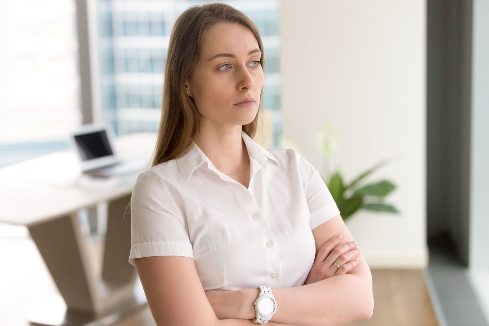 pensive businesswoman standing with arms crossed in modern office interior