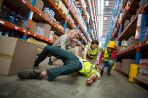 Workers taking care about their colleague injured by a slip and fall lying on the floor in a warehouse