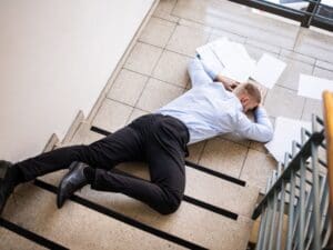 man lying at the bottom of a stair case with papers scattered around him