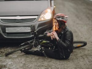Cyclist wearing a helmet sitting in front of a car with their bicycle on the ground