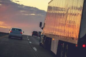 A large semi-truck traveling closely alongside passenger vehicles on a highway at sunset, representing the potential danger of truck accidents. Munley Law provides expert truck accident lawyers near you to help after a serious crash. For immediate assistance, call Munley Law at 855-866-5529.