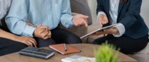An attorney’s hands hold a tablet displaying legal documents while a couple sits in the background, representing the case review stage of the process of filing a personal injury lawsuit in Allentown. This image highlights Munley Law’s personalized approach in their Allentown office. Call844-686-5397 to arrange your case review for a personal injury lawsuit in Allentown, PA with Munley Law. It shows a warm, professional environment.