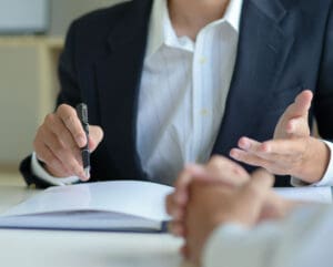 Lawyer writing notes while talking to a person clasping their hands together