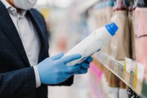 Man wearing protective rubber gloves and a mask reads the label of washing powder in store