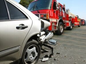 Car with rear end accident damage with three fire trucks parked behind it