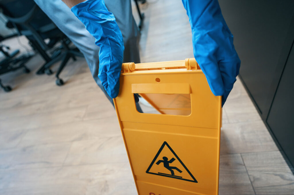 Worker in protective gloves puts up a yellow fold-out warning sign about a wet field