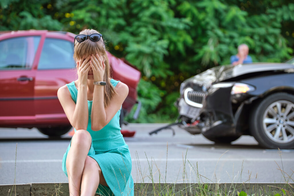 Stressed woman driver sitting on street side shocked after car accident. Road safety and insurance concept.