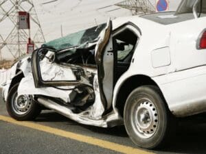 Severely damaged white sedan illustrating extensive side-impact collision damage, typically associated with accidents involving uninsured motorists in Allentown, Pennsylvania. Munley Law, located in Allentown, PA, at (855) 866-5529, specializes in handling car accident claims involving uninsured drivers. The image clearly shows significant damage to the vehicle's doors and frame, highlighting the potential severity and financial implications of uninsured motorist accidents. The accident scene is set on an asphalt road with debris around the damaged vehicle, emphasizing the importance of experienced legal assistance after such incidents.