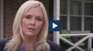 Close-up image of a Philadelphia workers compensation attorney from Munley Law speaking outdoors. The attorney has light blonde hair and is standing in front of a brick building with a white porch railing. This still image represents a testimonial or informational video about workers' compensation rights in Philadelphia.