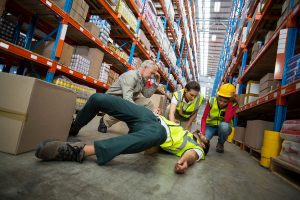 Workers taking care of their colleague lying on the floor in a warehouse