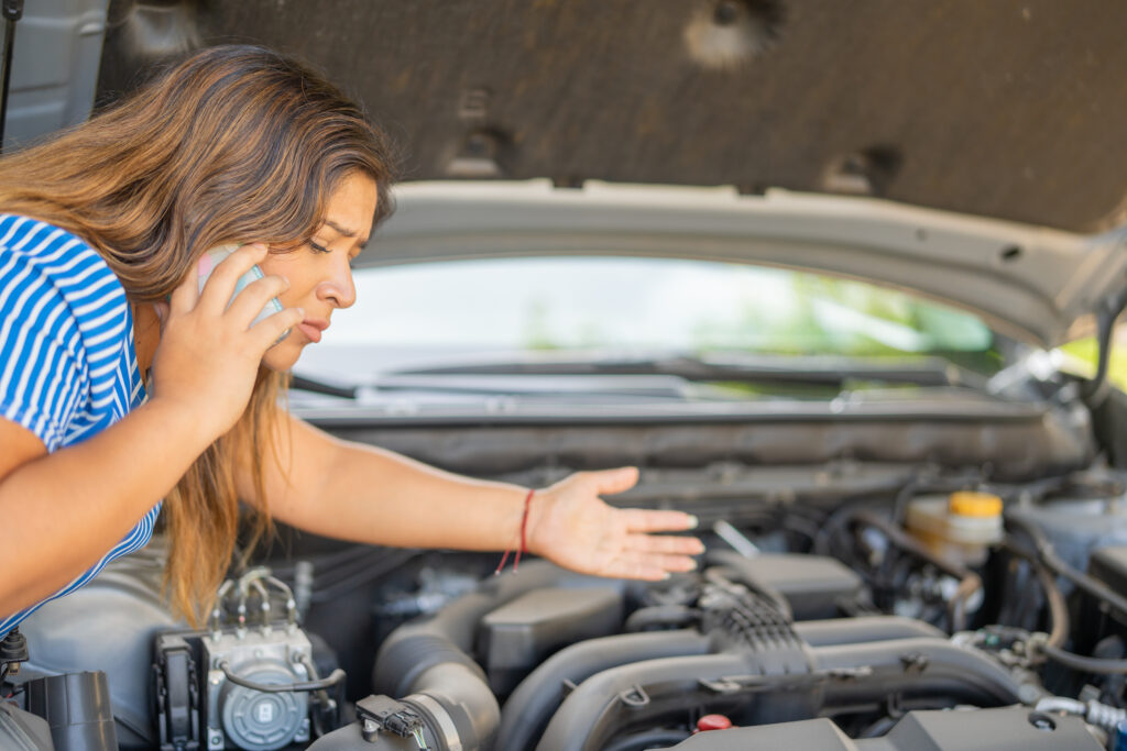 Worried woman looking at her car engine and asking for help for mechanical problems, with the engine hood open.